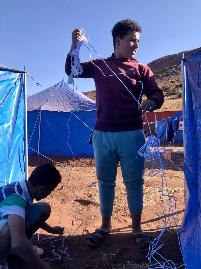 Mohammed, habitant du village de Tizi N’Oucheg, touché par le séisme qui a frappé le Maroc, installe un kit solaire sur les tentes qui abritent les villageois.